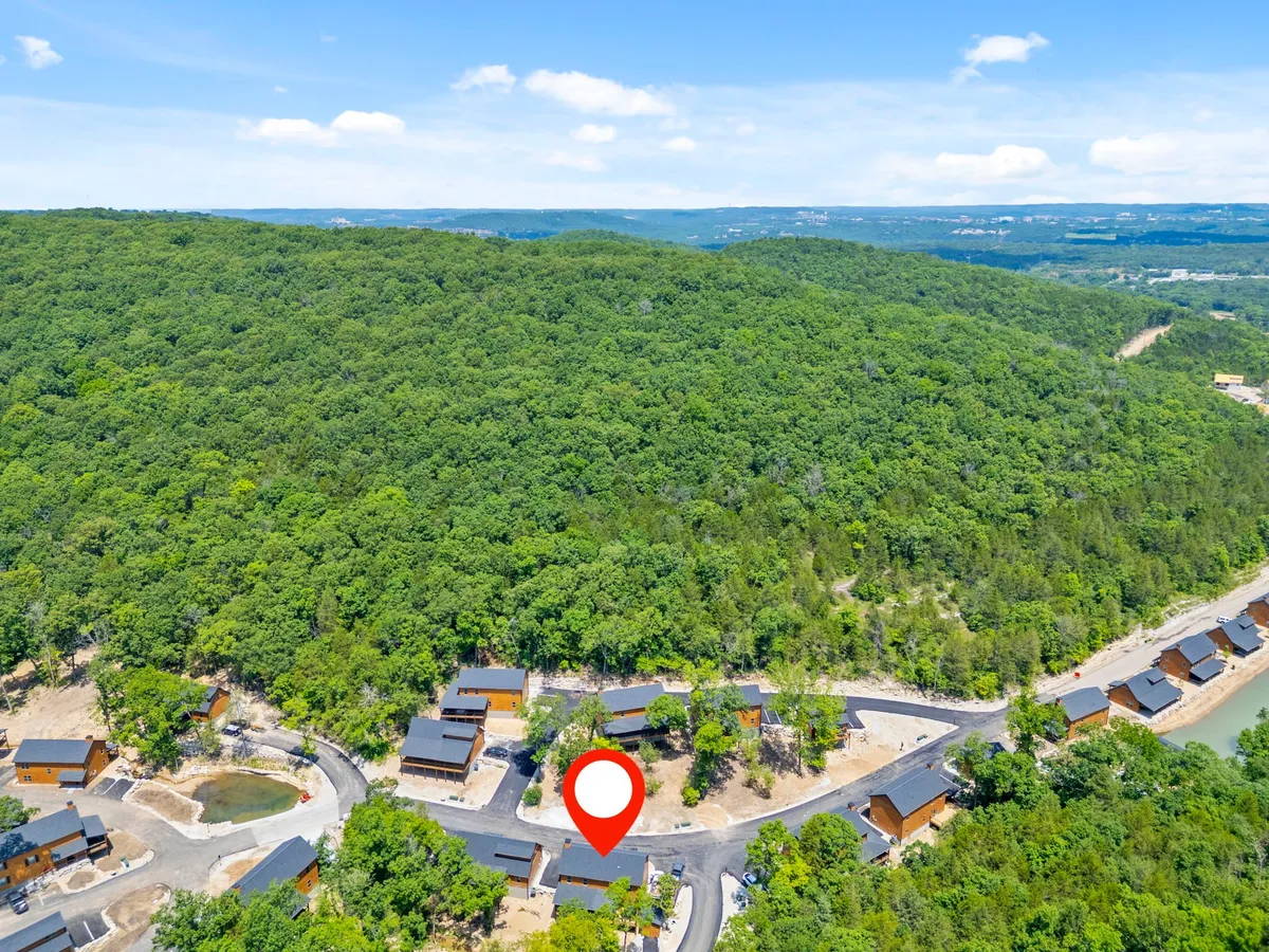 A tranquil scene featuring a lush green hillside dotted with cabins and a winding road weaving through the landscape. The peacefulness and connection to nature are palpable, hinting at outdoor exploration and relaxation opportunities.