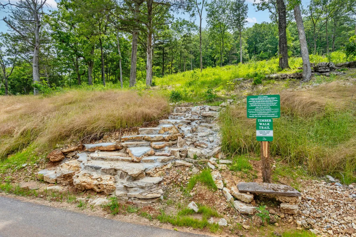 A set of stone steps leads up past a trail sign into a lush, green wooded area, emphasizing hiking opportunities. The image invites the viewer to imagine setting out on an adventure along scenic resort trails, with the promise of discovering local wildlife and seasonal flora.