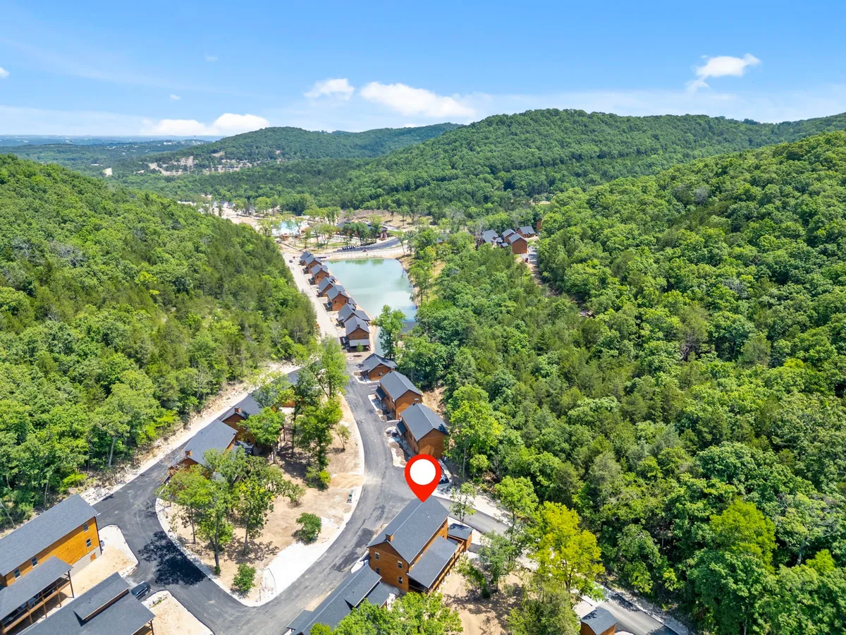 A serene natural setting featuring wooden cabins nestled beside a tranquil lake, surrounded by lush greenery and a winding road. The scene suggests opportunities for fishing, hiking, and peaceful relaxation by the water.