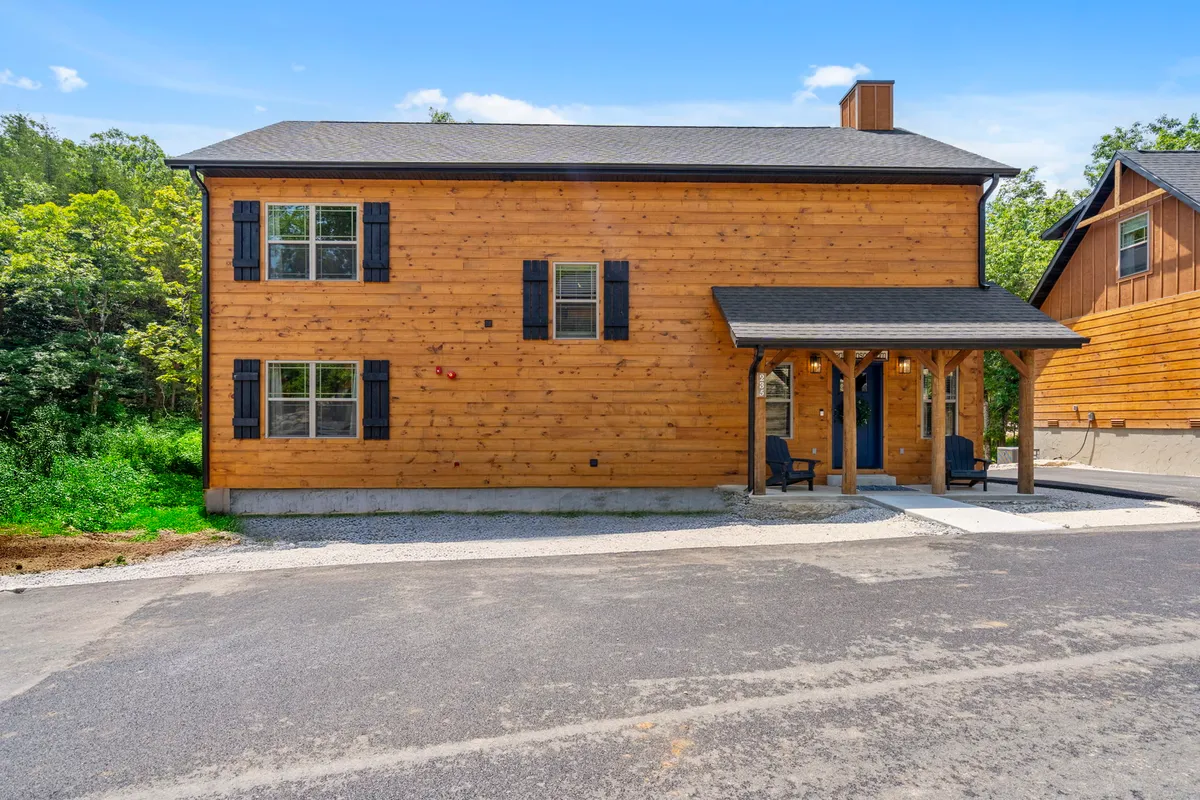 A welcoming view of the home's wooden exterior, complete with inviting black shutters and a spacious front porch surrounded by trees. The scene captures a serene moment with natural light and hints at the cozy, private space inside.