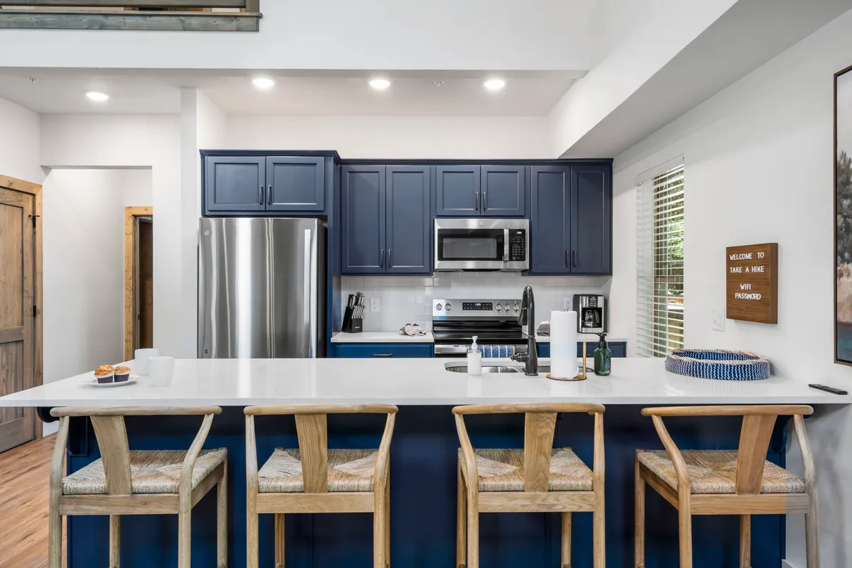 A modern and welcoming kitchen with blue cabinetry, a crisp white countertop, and bar stools lined up for casual conversation or snacking. The space is ready for cooking, baking, or hosting family around the island.