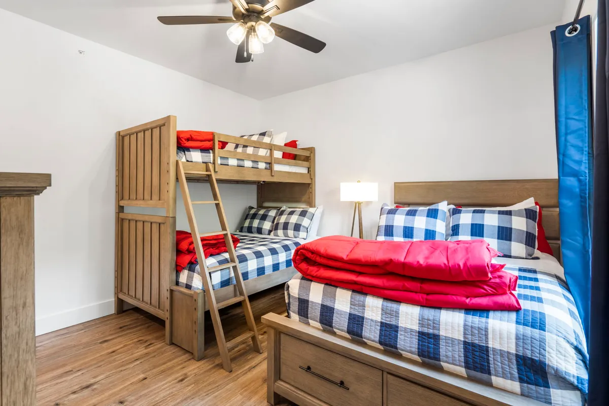 A playful bunk room with a bunk bed and a separate bed featuring checkered and red bedding. Wooden furniture and a bright atmosphere make it perfect for kids or extra guests, capturing a sense of fun and flexibility.