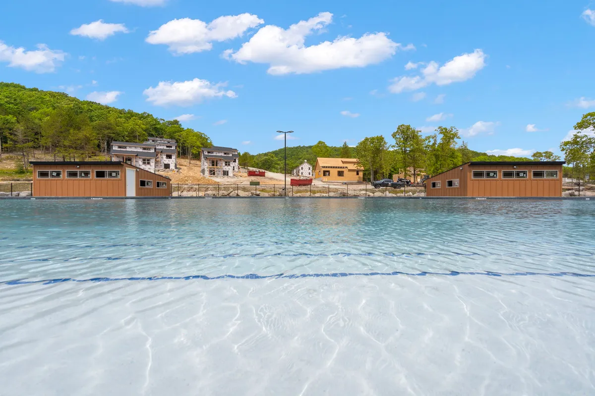 A serene lake sits in the foreground with a natural landscape and some buildings in the background. The water’s surface reflects the sky, and the setting feels calm and inviting, evoking the tranquility described for fishing, boating, or picnicking by the water.