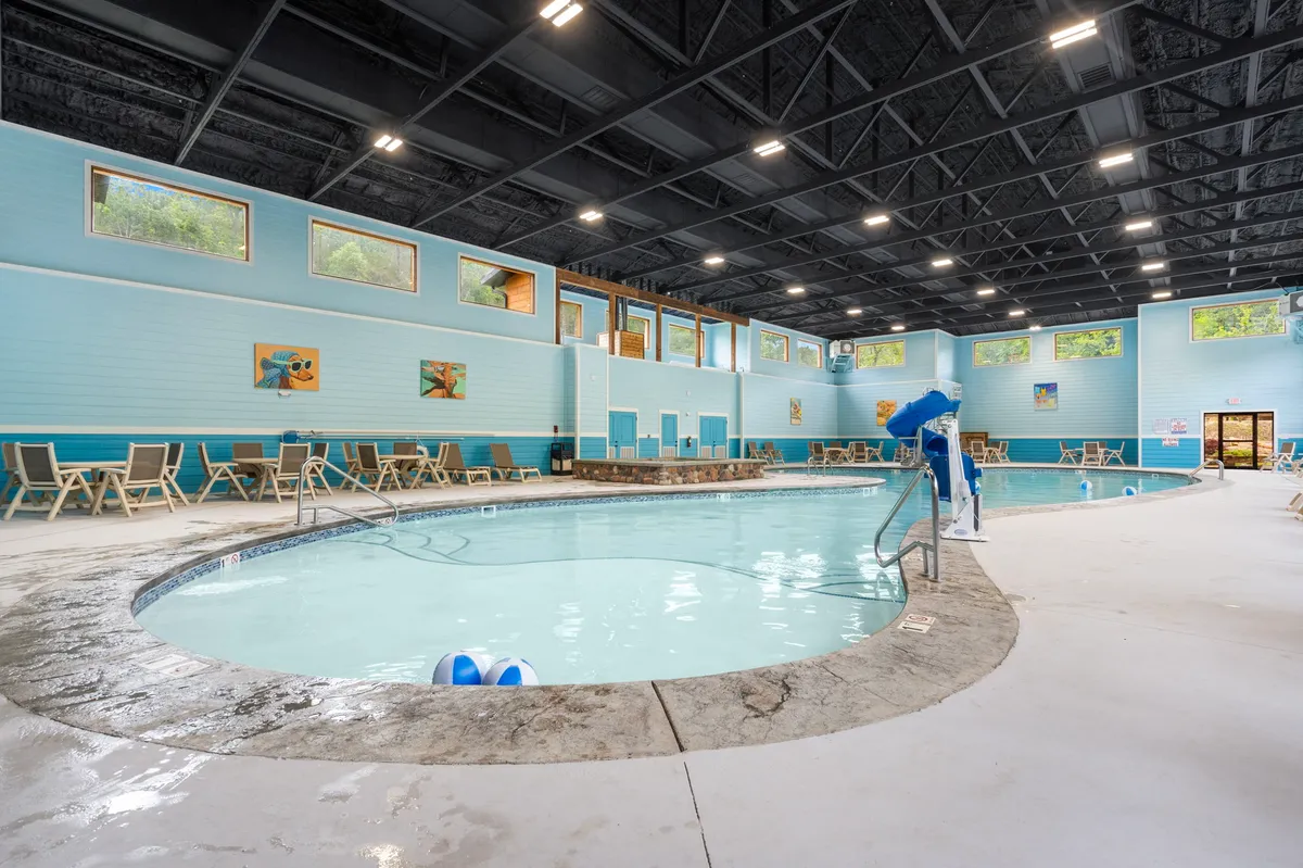 An inviting indoor swimming pool area featuring clear blue water, lounge chairs, and large windows that flood the space with sunlight. Decorative wall art adds a cheerful touch. The scene is perfect for families enjoying swimming and poolside games together, regardless of weather.