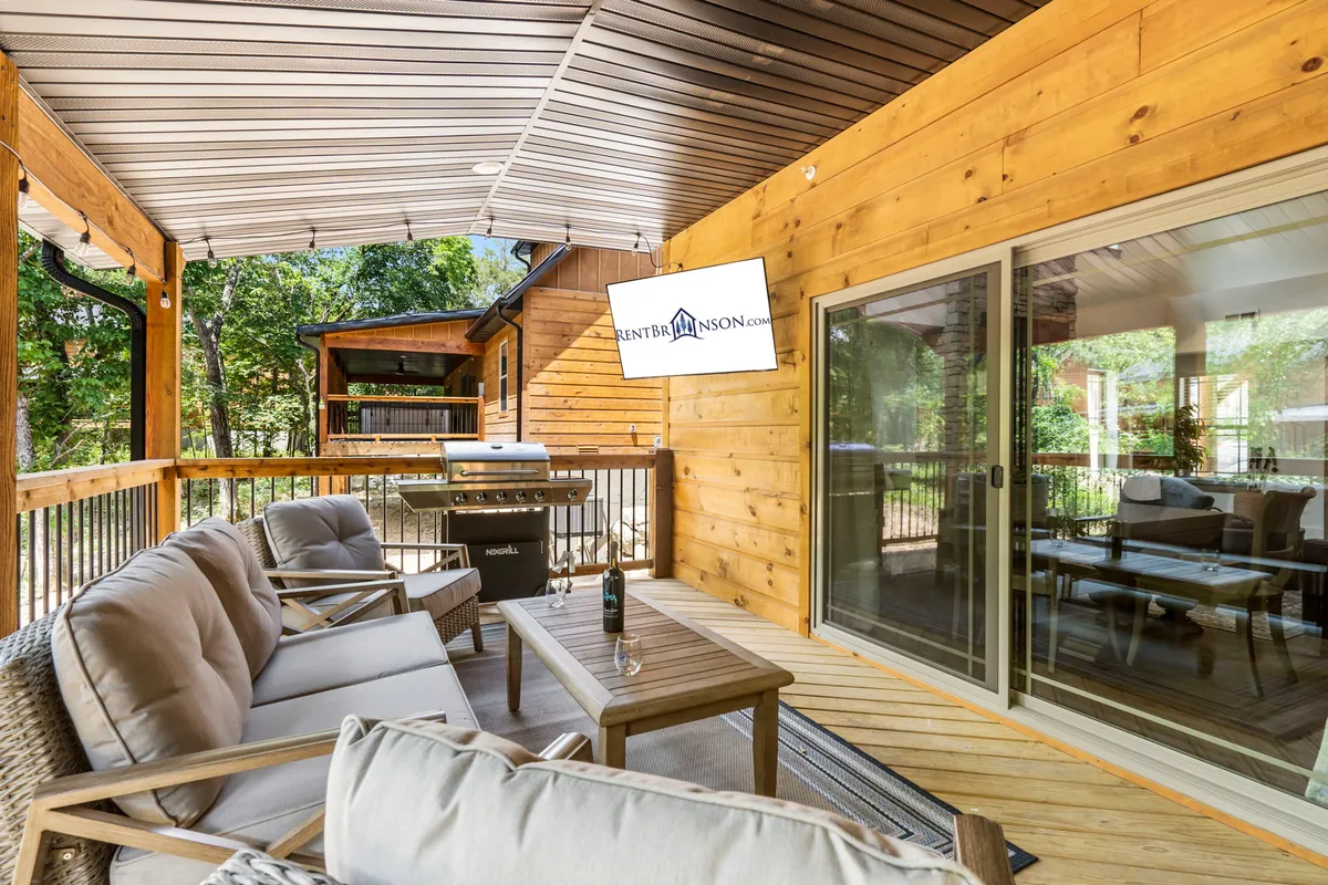A cozy outdoor area with a comfortable seating arrangement and a grill setup, framed by a decorative wall and surrounded by greenery. The scene suggests relaxed barbecues, casual gatherings, or peaceful mornings spent outdoors.
